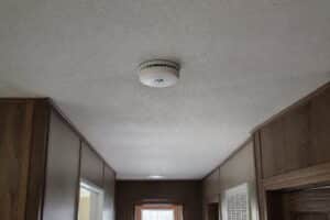 Smoke detector mounted on a hallway ceiling inside a manufactured home